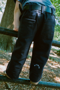 Child wearing navy pants with a brand logo, standing on a metal railing in a natural setting.