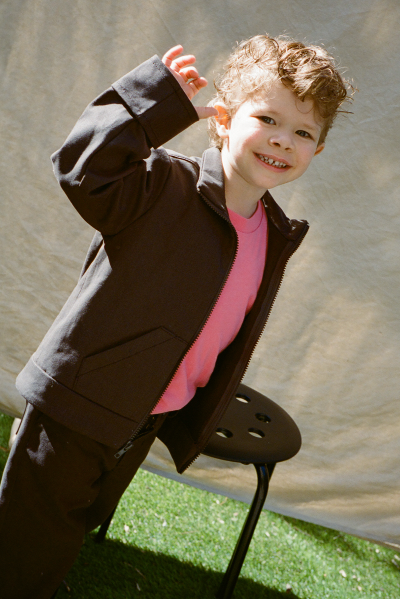 Child in a jacket standing on a chair with a neutral background