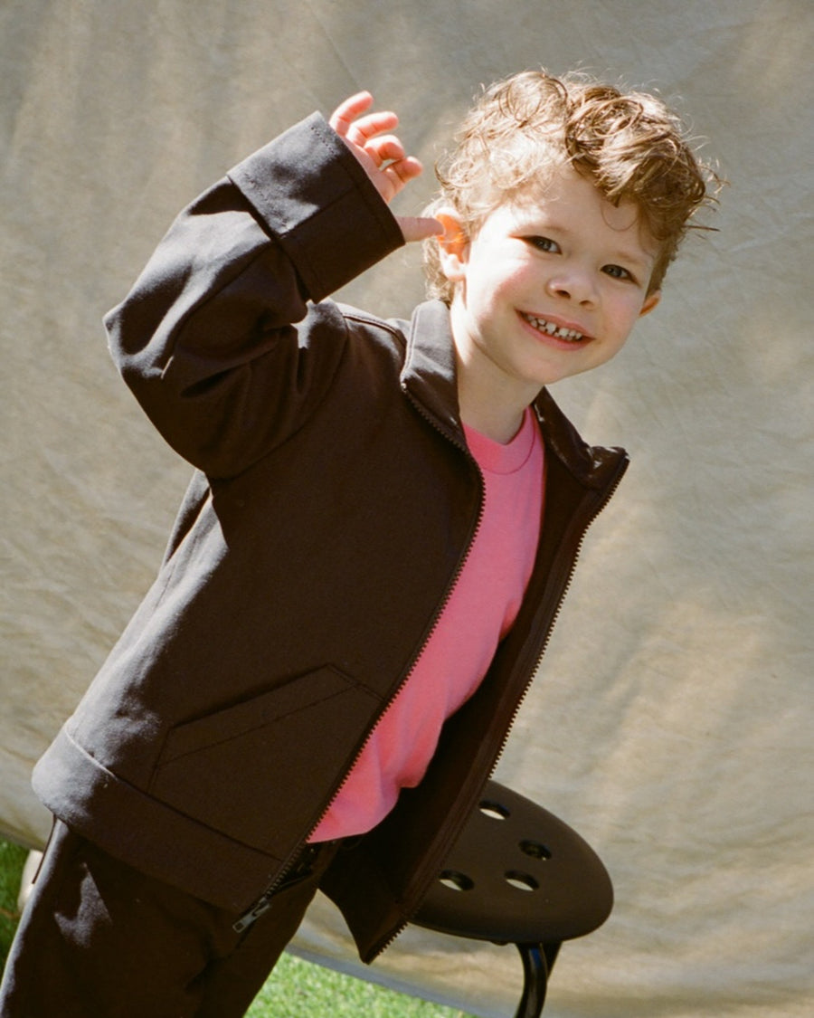 Child in a jacket standing on a chair with a neutral background
