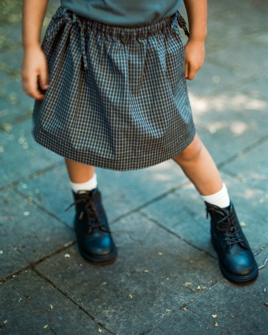 Child wearing a blue shirt, plaid skirt, and black shoes on a pavement.